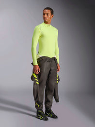 Alpinestars ZX Evo V3 Top - Long Sleeve, Yellow Fluo, worn by a model with a dark grey racing suit tied at the waist and black racing boots, flame-resistant motorsport base layer, lightweight jacquard mesh construction, professional auto racing gear