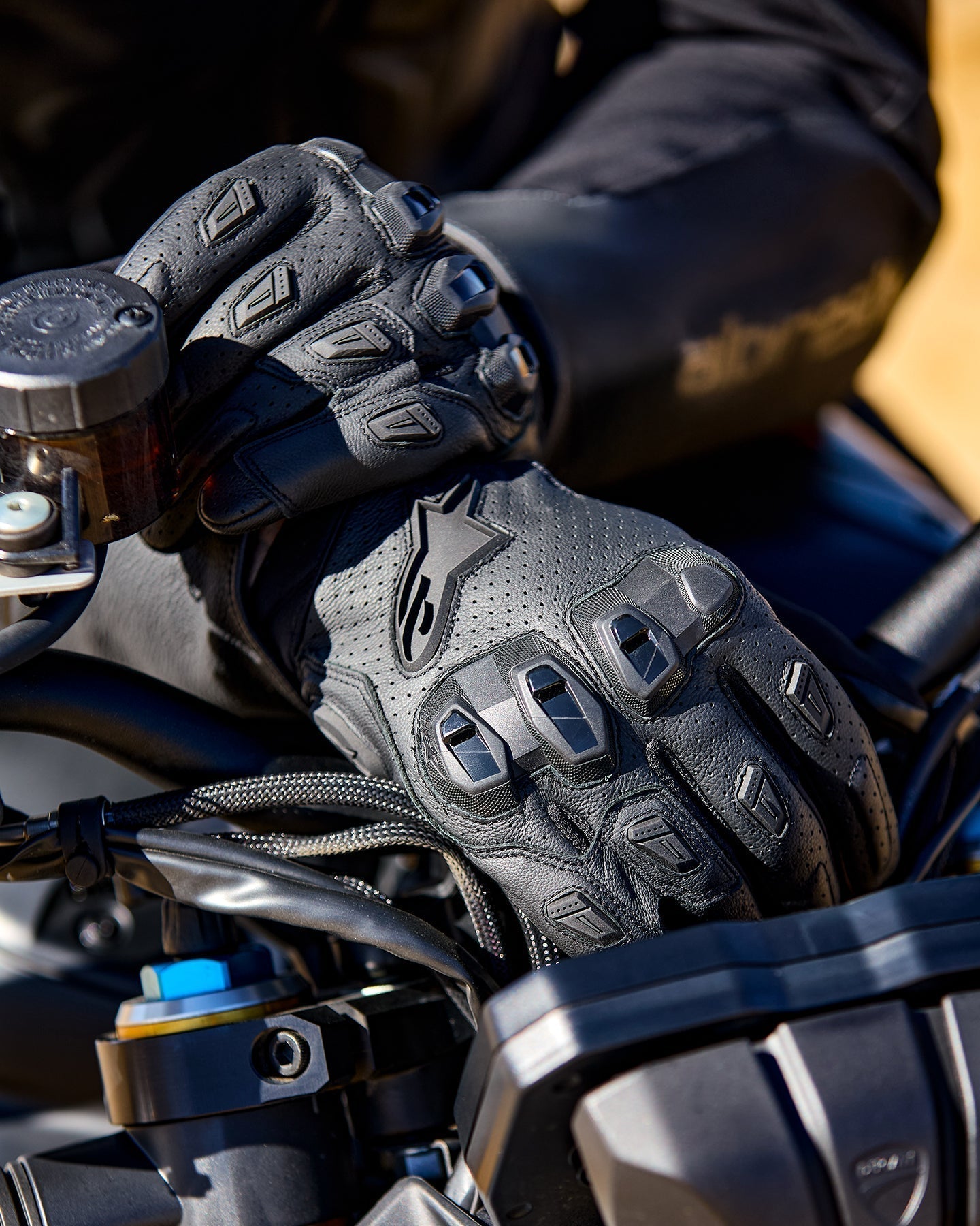 Alpinestars SP X 7 black perforated leather motorcycle gloves with TPU knuckle protection on motorcycle handlebars.