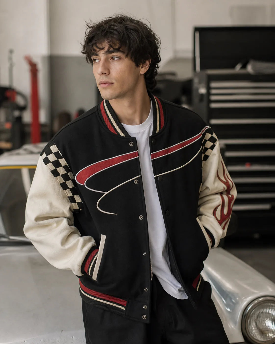Young adult wearing a black cream and red racing varsity jacket in a garage