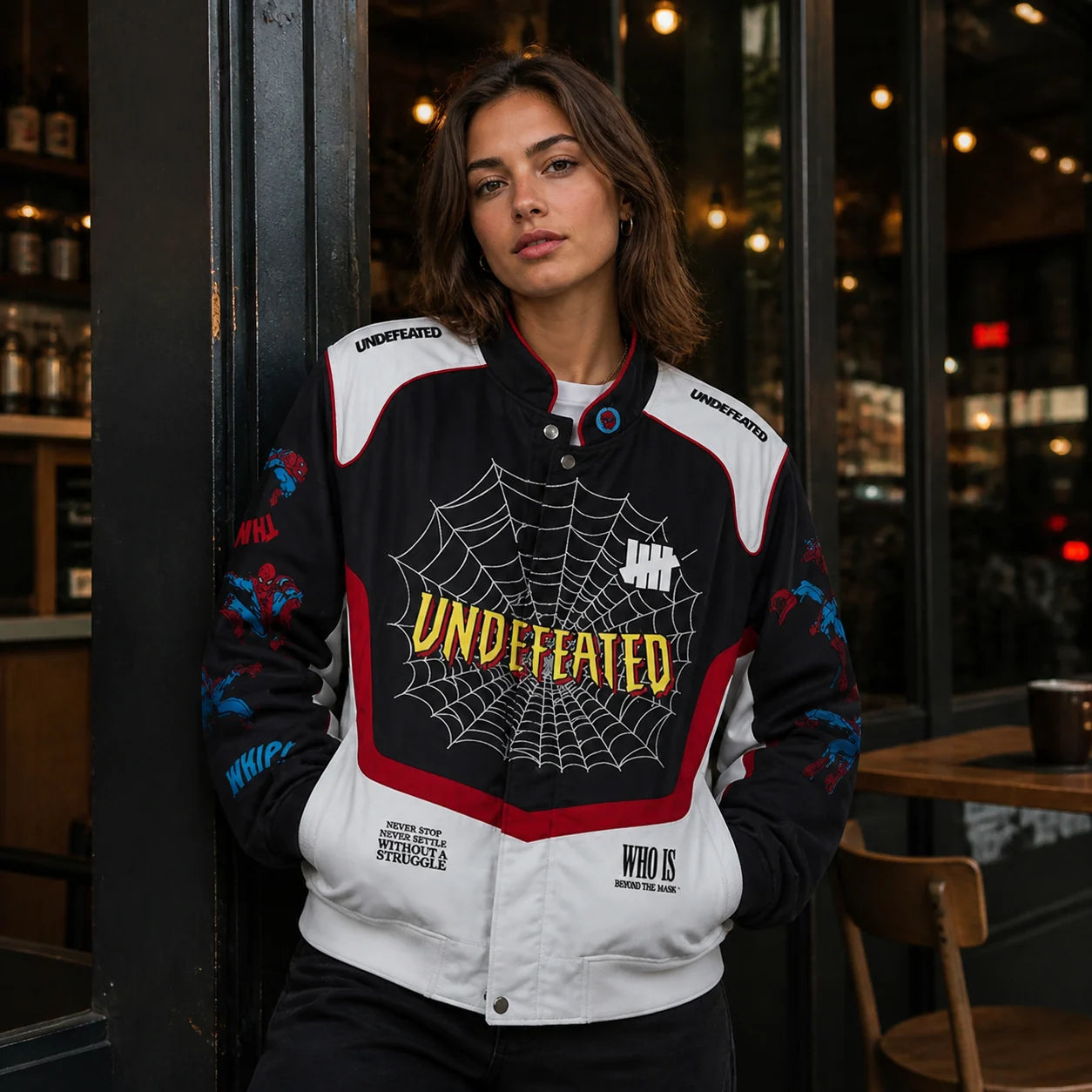 Adult woman in the black white and red Undefeated Spider-Man varsity jacket outside an urban cafe at night