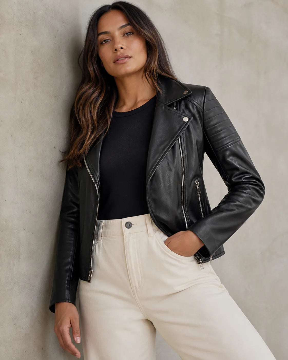 Woman styling a black leather moto jacket in a neutral studio setting